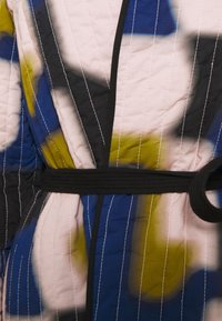 Kevlar nhẹ dạng chần bìa màu xanh, hồng và vàng với các điểm nhấn màu đen; có đường chỉ dọc và dây thắt lưng màu đen.