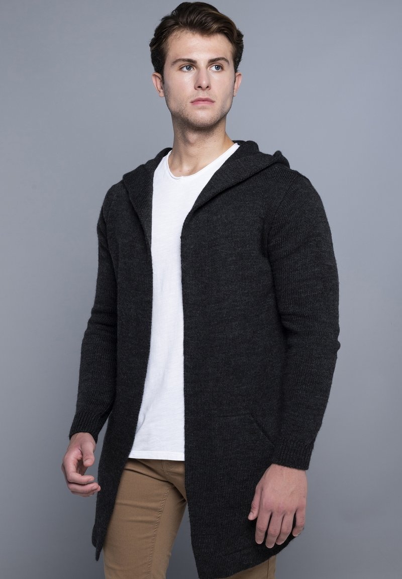 Donkergrijze gebreide cardigan met een capuchon, lange mouwen en zijzakken. Draag je over een wit shirt met een rechte snit en een gestructureerde stof.