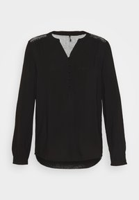Blouse noire à manches longues avec un col rond, patte de boutonnage verticale et accents d'épaules transparents et à motifs. Tissu lisse, coupe décontractée.