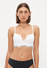 Witte naadloze beha met een diep decolleté, verstelbare banden en een Calvin Klein-logo band. Gladde textuur en minimalistisch ontwerp.