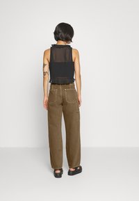 Svart ärmlös topp med volangkant, parat med löst sittande bruna cargobyxor med bakfickor och synliga sömmar.