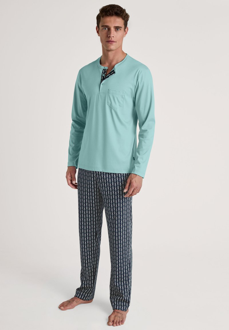 Lichtblauw langemouwen top met een zak en een patroon op de henley hals, gecombineerd met donkerblauwe broek met een witte geometrische print.