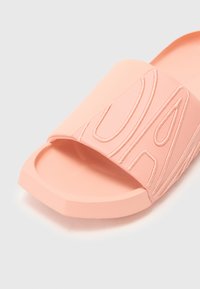 Pink slide sandal with a wide strap featuring textured lettering. Flat sole with a slightly raised edge. Matte finish and soft material.