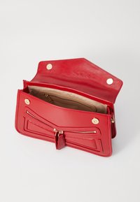 Röd läderhandväska med en glansig finish, zippered fack, guldfärgade detaljer och beige foder inuti. Har en strukturerad design.