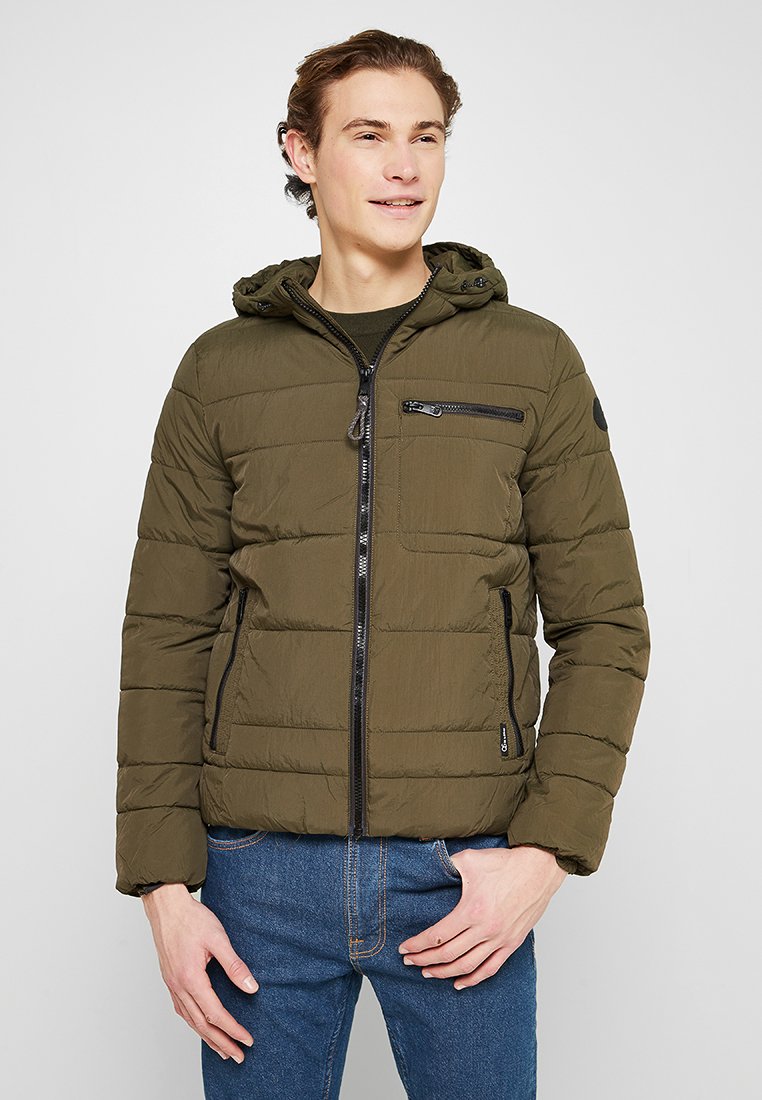 Olijfgroene pufferjack met capuchon, ritssluiting aan de voorkant en borstzak, ribbels aan de mouwen en een gestructureerde afwerking. Zwarte accenten op de ritsen.