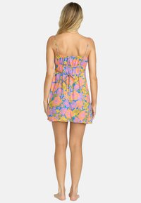 Bloemendress met dunne spaghettibandjes, voorzien van een geplooid taille en een levendig patroon van roze, paarse en gele bloemen op een lichte achtergrond.