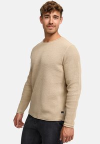 Beige gebreide trui met een textuurpatroon, ronde halslijn en lange mouwen. Bevat een klein logo-label aan de onderkant.