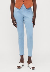 Lyseblå skinny jeans med høy midje, med sømløst design og frynset kant, sammen med hvite sandaler med blokkhæl.