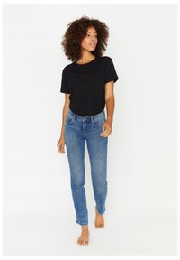 T-shirt nera a maniche corte abbinata a jeans blu attillati. I jeans presentano un classico design a cinque tasche e una texture leggermente scolorita.