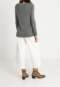 Pull gris texturé à manches longues avec un col plongeant, associé à un pantalon blanc à jambes larges et des bottines marron à motif serpent.
