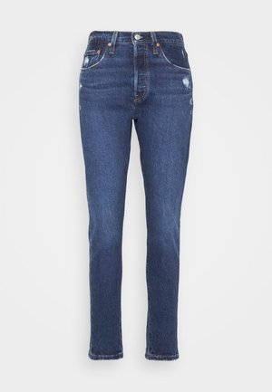 Jean en denim bleu foncé avec une coupe droite classique, présentant une légère usure, cinq poches et une taille standard avec un bouton en métal.