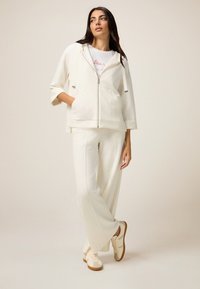 Felpa a zip color crema con motivo a pois, pantaloni dal taglio rilassato e sneakers di colore chiaro. Tessuto morbido e design casual per il massimo comfort.