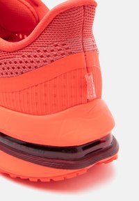 Λαμπερό πορτοκαλί αθλητικό παπούτσι με υφασμάτινο άνω μέρος με υφή, μαξιλαρωμένο τακούνι, γυαλιστερή μαύρη σόλα και μια μικρή ετικέτα στο πίσω μέρος για εύκολη χρήση.