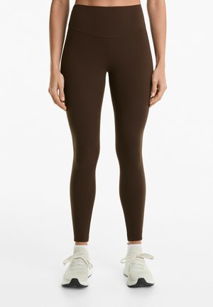 Brown high-waisted leggings with a smooth texture, fitted design, and no visible patterns, paired with light-colored athletic shoes.