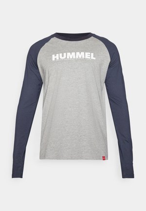 Šedé tričko s dlhými rukávmi a námorníckymi raglánovými rukávmi, s bielym potlačeným textom "HUMMEL" cez hruď; mäkká látka a voľný strih.