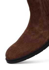 Stivale alla caviglia in suede marrone con punta tonda e suola in gomma nera. Presenta dettagli di cucitura discreti lungo i lati.