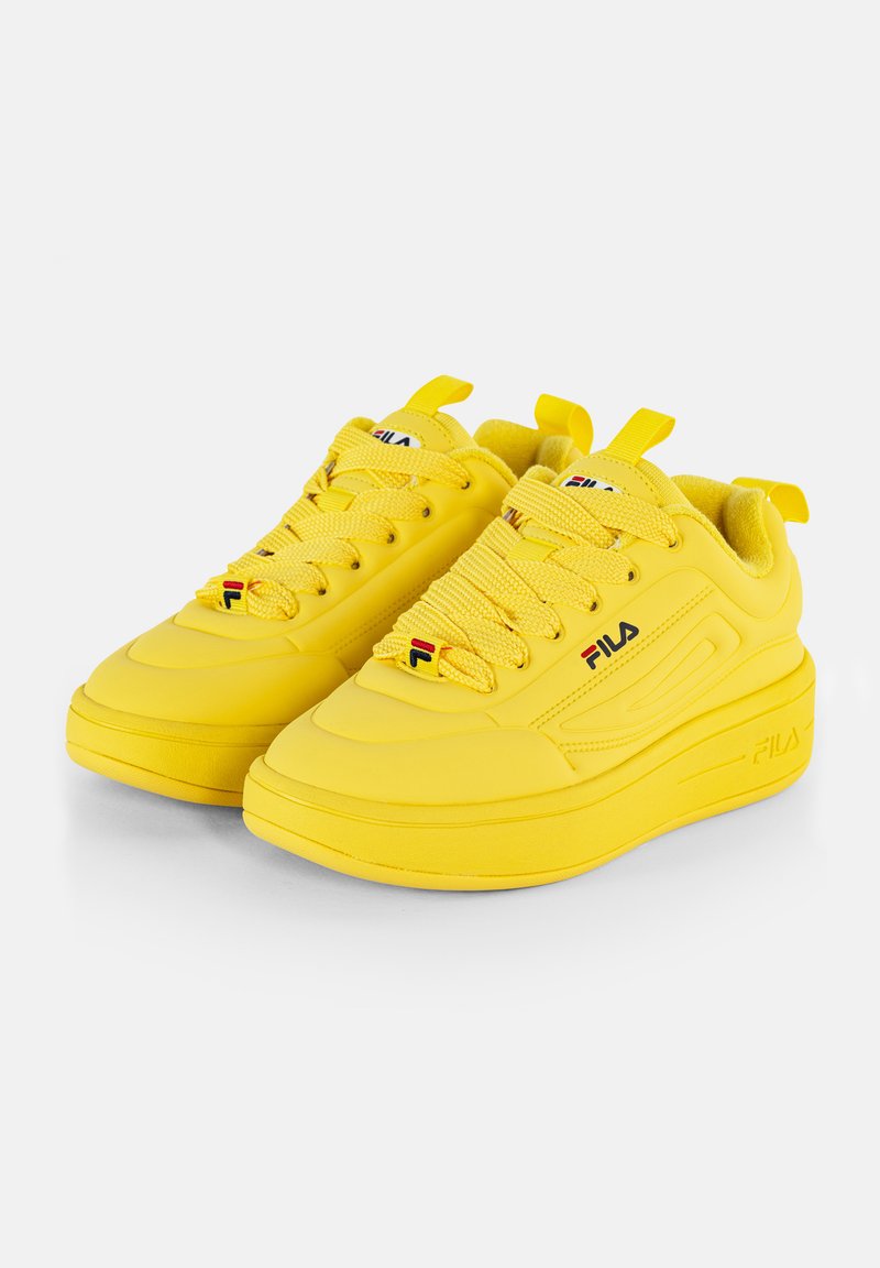 Zapatillas FILA amarillas con lengüeta acolchada, cordones texturizados y suela gruesa. Presenta un pequeño logotipo en la lengüeta y en el panel lateral.