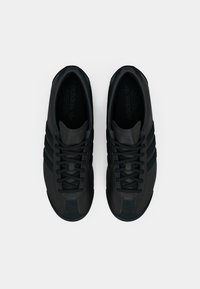 Črni atletski čevlji z elegantno zasnovo, gladkim usnjenim materialom, šestimi zankami za vezalke, tremi črtami na strani in teksturiranim prednjim delom čevlja.