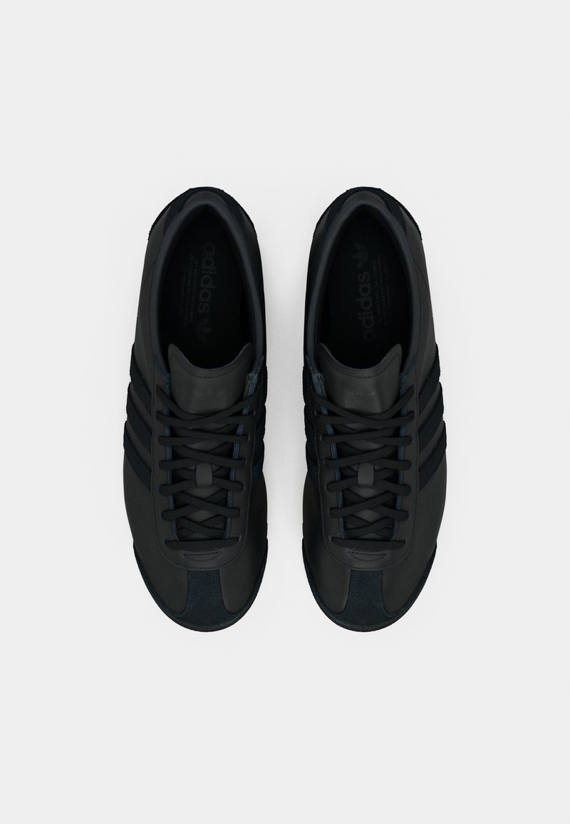 Black athletic shoes featuring a sleek design, smooth leather material, six eyelets, three side stripes, and a textured toe cap.