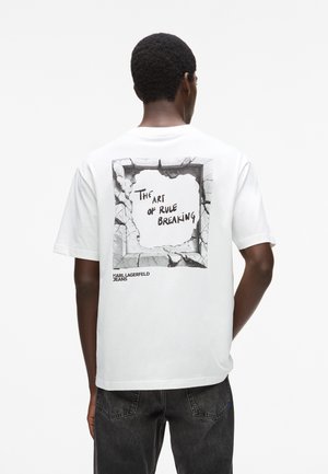 Mann trägt ein weißes T-Shirt mit einem abblätternden Wandgrafik und dem Text „The art of rule breaking“ und „Karl Lagerfeld Jeans“ auf der Rückseite.