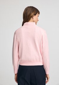 Rosa tröja med hög krage, räfflad nederkant och långa ärmar, tillverkad av mjukt material med en slät textur.