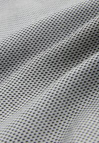 Gros plan d'un tissu gris plié avec un petit motif à grille noir et blanc répétitif créant une surface texturée.