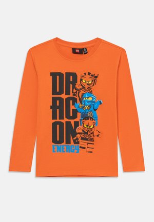 Orange langærmet t-shirt med et grafisk motiv af tre ninjas i blå og sort med teksten "DRAGON ENERGY" i fed skrift.