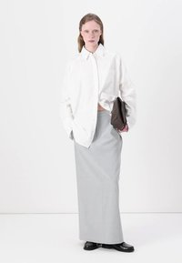 White oversized button-up shirt, gray fitted skirt, black pointed shoes, holding a brown handbag. Smooth fabric, minimalist design.