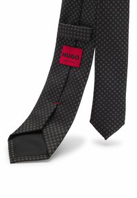 Schwarze strukturierte Krawatte mit einem Diamantenmuster. Mit einem roten "HUGO"-Label. Hergestellt in Italien, mit einer glatten, einfarbigen Rückseite.