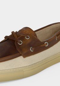 Καφέ δερμάτινο και μπεζ καμβά boat shoe με λεπτομέρεια κορδονιών που περνούν μέσα από ασημένιες θήκες και ανοιχτό μπεζ λαστιχένια σόλα.