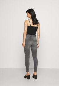 Jeans skinny cinzentos com cintura alta, feitos de denim. Têm um acabamento suave e bolsos traseiros. Combinam com uma blusa preta de alças e saltos altos.