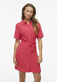 Korálové šaty s krátkymi rukávmi a gombíkovým zapínaním, s opaskom na cinčovanie v páse a prednou vreckom. Hladká textúra, voľný strih, dĺžka až po kolená.