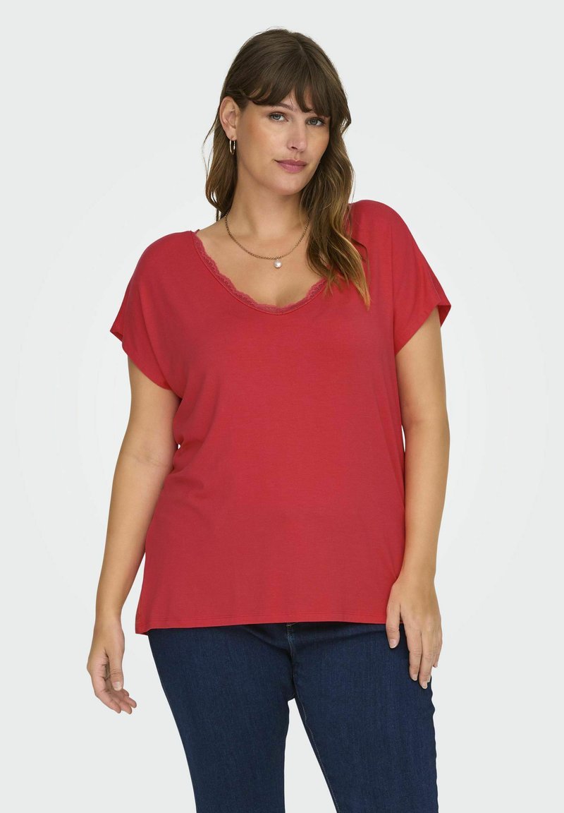 Červené tričko s krátkým rukávem a vlnitým výstřihem, volného střihu, vyrobené z měkkého materiálu, v kombinaci s tmavomodrými džíny.