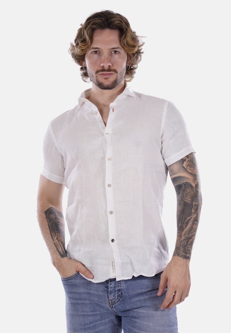 Camicia bianca in lino a maniche corte con bottoni sul davanti, caratterizzata da una sottile texture e piccoli dettagli rossi. Indossata con jeans azzurri chiari.