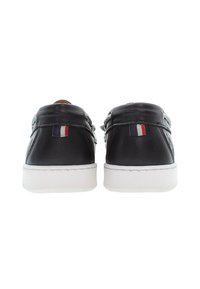 Svarta läderskor med vit sula, med justerbara remmar och en liten tri-färgad accent nära hälen. Slät textur och låg profil.