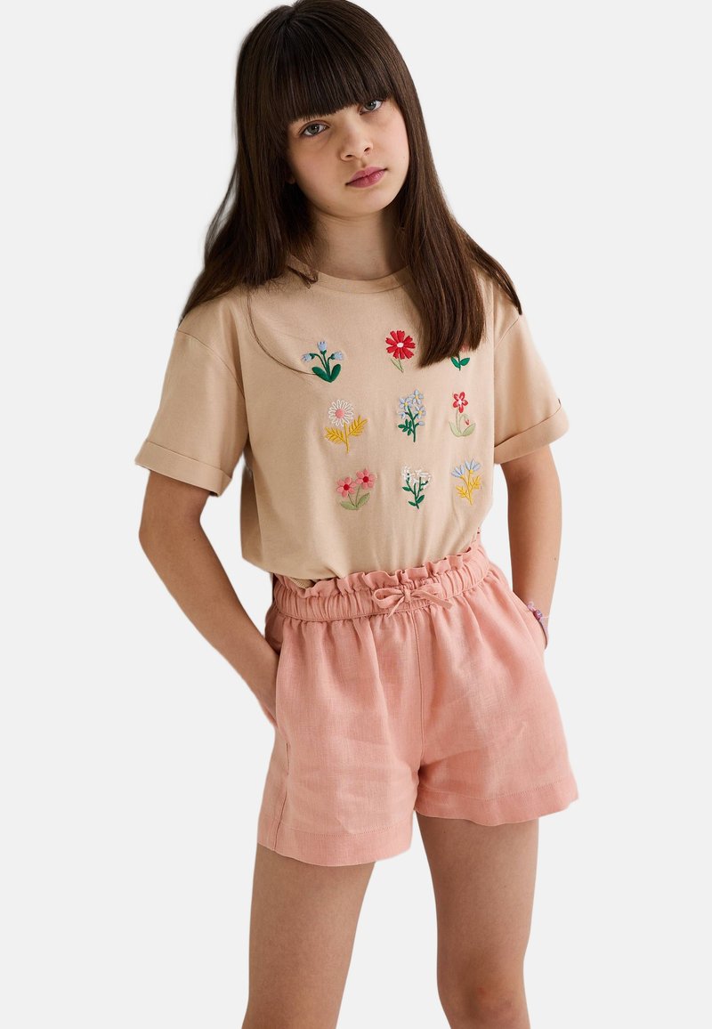 T-shirt en coton beige avec broderies florales, associé à un short en lin rose clair avec une taille élastique et des poches latérales.