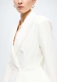 White blazer with a tailored design, double-breasted style, smooth texture, and round buttons. Features sharp lapels and clean lines.