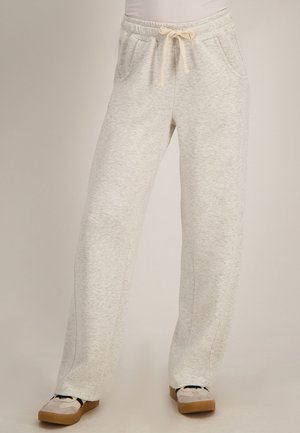 Lichtgrijze sweatpants met elastische tailleband en crèmekleurige trekkoorden, gedragen met lichte sneakers met bruine zolen.