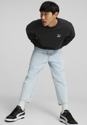 Svart hettegenser med hvitt logo, lyseblå tapered jeans og svarte sneakers med hvite detaljer. Casual, avslappet passform med klassisk design.