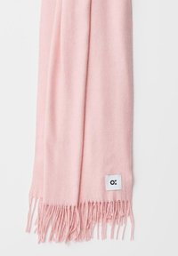 Écharpe rose en matière douce, avec des franges aux extrémités et une petite étiquette de logo blanche près du bord inférieur.