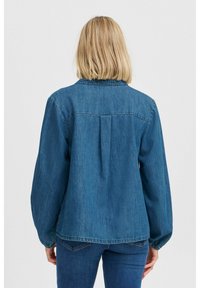 Giacca di denim blu medio, con una vestibilità rilassata, dettaglio di piega sottile sul retro e maniche lunghe con polsini elasticizzati.