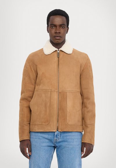 Chaqueta de ante marrón con un cuello de borreguito blanco, cierre de cremallera y dos bolsillos delanteros. Presenta un diseño ajustado y una textura suave.