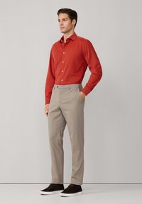 Camisa roja de manga larga con botones, combinada con pantalones de patrón gris claro y zapatillas marrón oscuro, presentando un corte relajado y detalles sutiles.