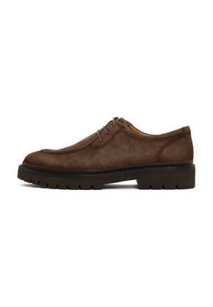 Zapato de ante marrón con cordones, suela gruesa de goma negra y surcos profundos, mostrado de perfil sobre un fondo blanco.