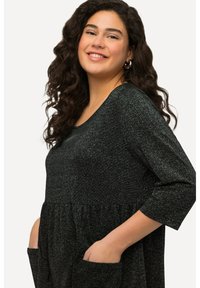Robe noire avec une finition texturée et brillante, à manches trois-quarts et taille froncée. Elle possède deux poches latérales pour plus de commodité.
