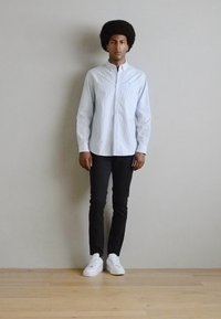 Hvid langærmet stribet skjorte i sydd pasform, parret med sorte slim-fit bukser og hvide sneakers. Enkel design med minimal hardware aksenter.