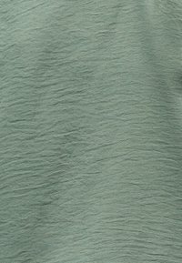 Φωτεινό πράσινο ύφασμα με διακριτικό υφή μοτίβο από ακανόνιστες οριζόντιες και κάθετες γραμμές που δημιουργούν κυματιστή επιφάνεια.