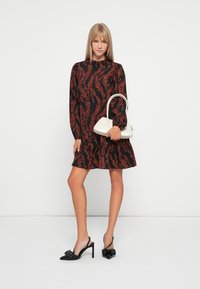 Black dress with red abstract patterns, long sleeves, and ruffled hem. Paired with a white handbag and black heeled sandals.