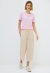Light pink cotton t-shirt with red lettering paired with cream wide-leg pants featuring a drawstring waist and textured fabric. White sneakers.