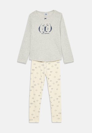 Grauer Langarmshirt mit zwei navyblauen Pinguin-Illustrationen und dem Text "Petit Bateau", kombiniert mit cremefarbenen Leggings, die mit kleinen Pinguinen gemustert sind.